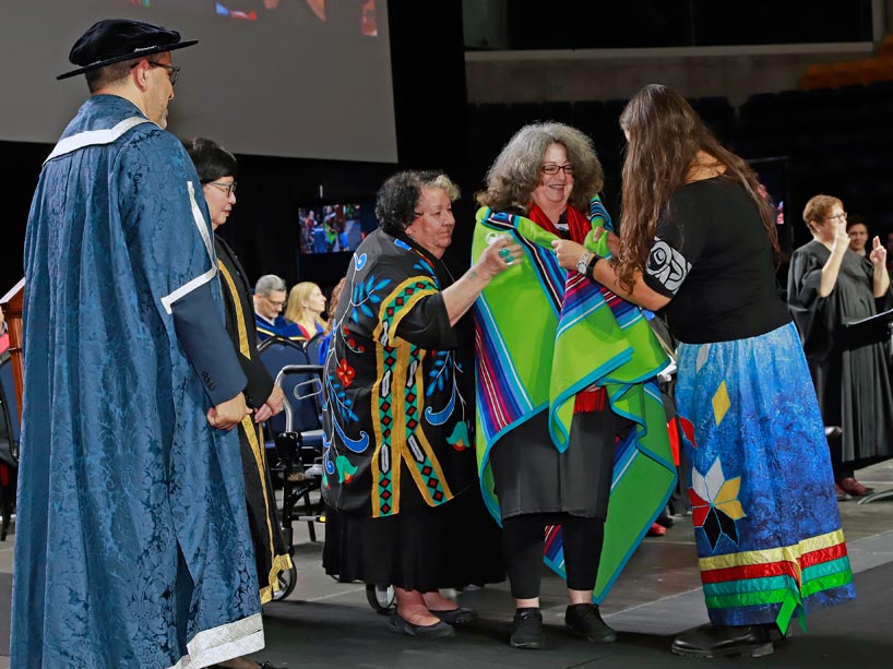 From left: President Mohamed Lachemi and Janice Fukakusa watch as Elder Joanne Dallaire (third from left) and Bobbi-Jo Virtue (right) drape a blanket over Deborah Smith (centre)