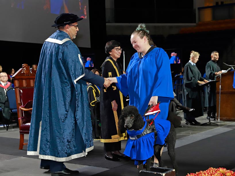 From left: President Mohamed Lachemi shakes Michelle Woolfrey’s hand while she holds her guide dog’s harness