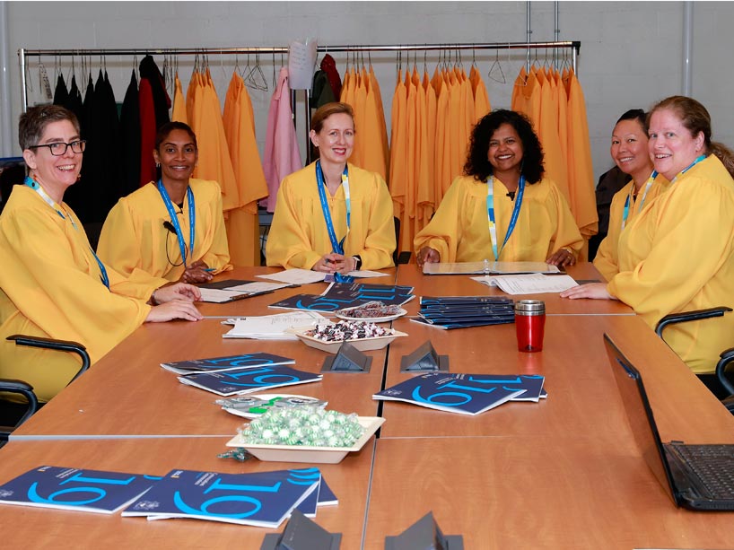 Six volunteers wearing yellow gowns sit around a table