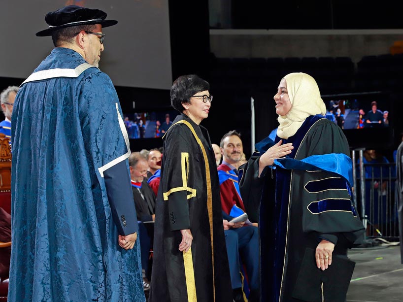 From right: A new graduate places her hand over her heart in greeting President Mohamed Lachemi (left) on stage at convocation