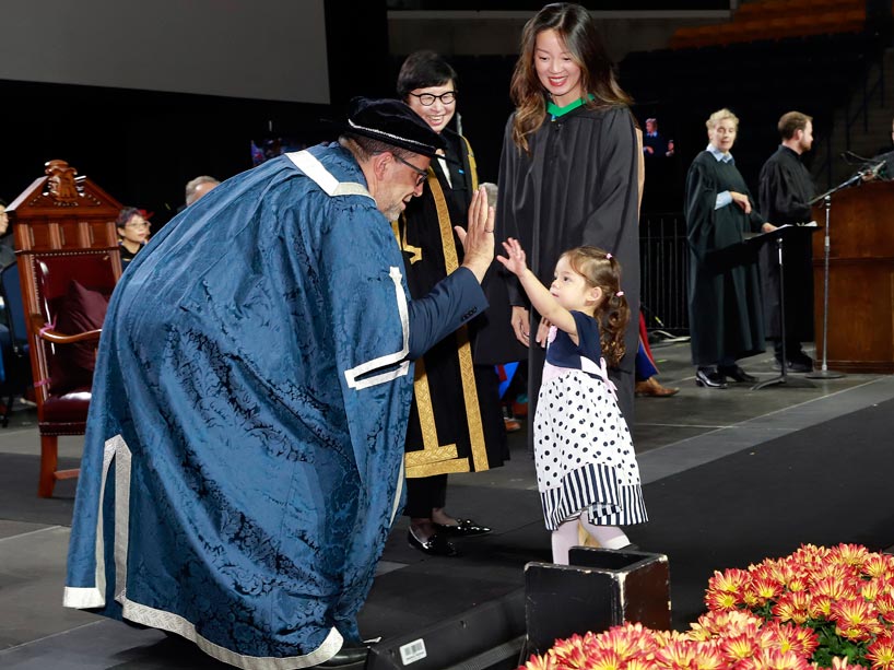 From left: President Mohamed Lachemi high fives the daughter of a graduate, who holds her other hand on stage at convocation