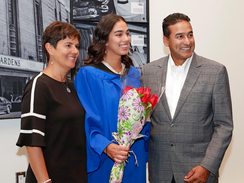 Parents flank their daughter, who holds roses and wears a blue convocation gown