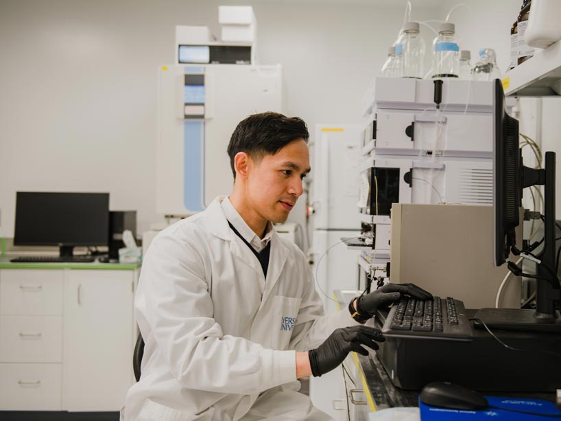 A man sitting at a computer wearing a lab coat and black rubber gloves