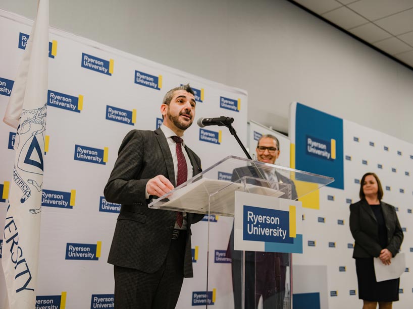 Minister speaks behind podium. Backdrop and podium show several Ryerson logos