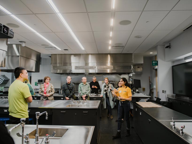 Student tour guide wearing a yellow t-shirt shows participants large demonstration kitchens