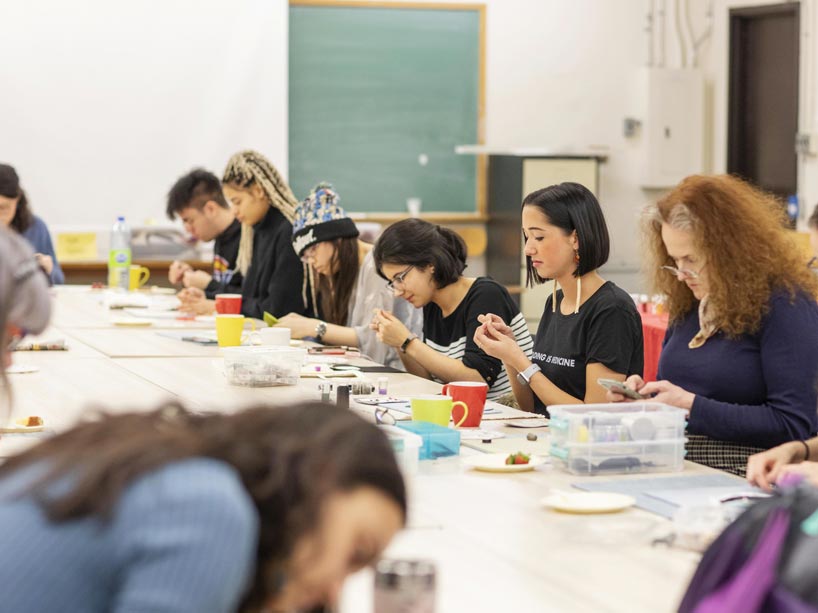 A group of people are seated around a table, working on beading projects.