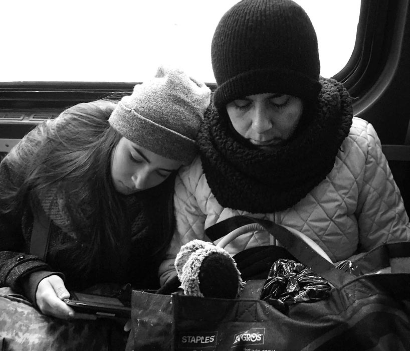Daughter leans on mother's shoulder, both sitting in subway train