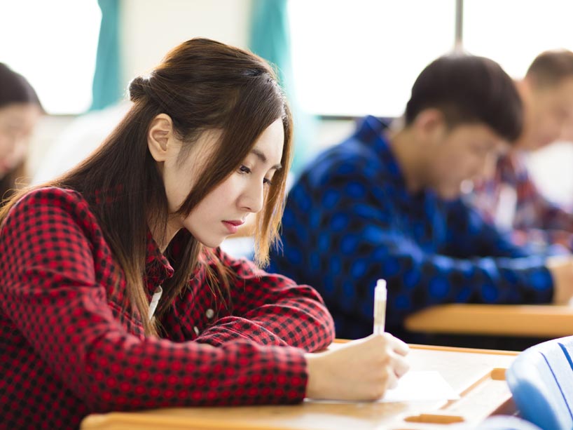 A student sits at a desk writing a test