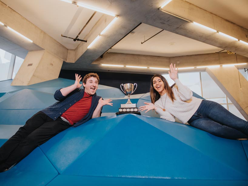 Male and female student lie on elevated platform with trophy in the centre