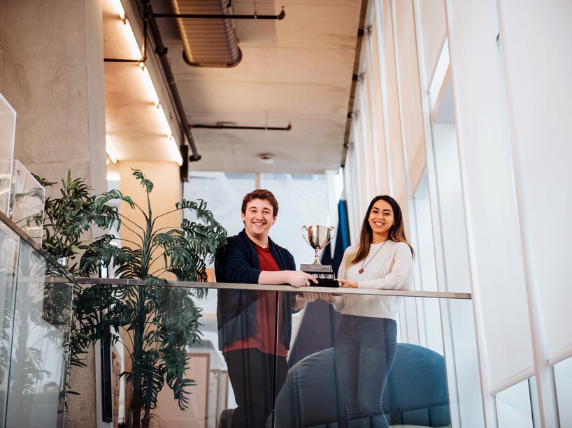 Male and female students standing and holding trophy over glass ledge