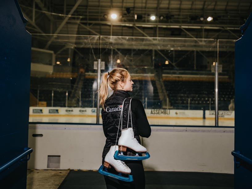 Young woman walks into stadium wearing a pair of ice skates over her shoulders