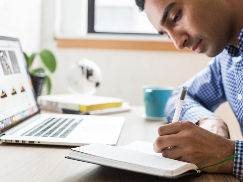 Man sitting at a desk and using a pen to write in a notebook