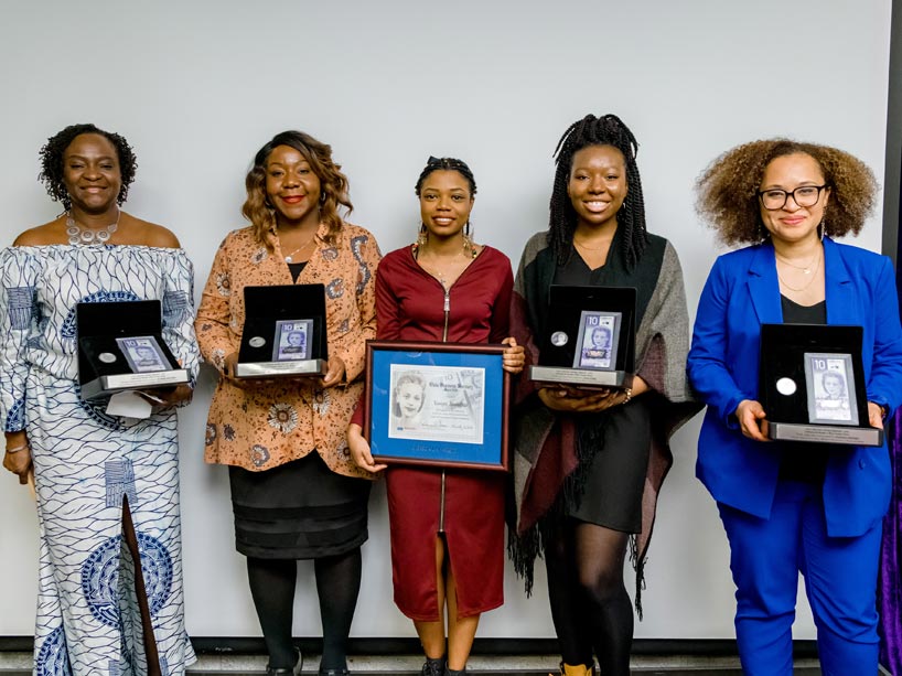 Five women holding award plaques standing side by side smiling