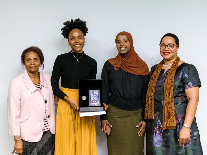 Four women standing side by side smiling with one of them holding an award