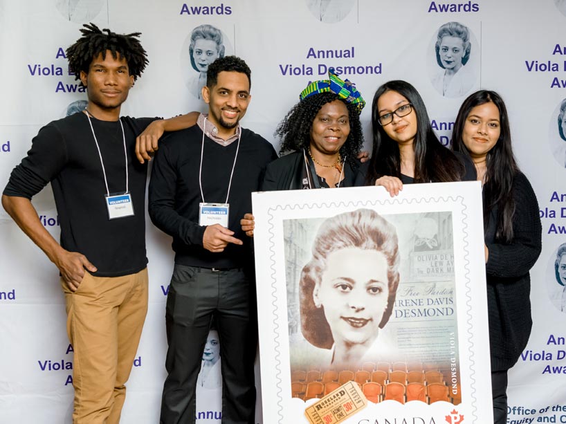 Five people standing behind a poster of the Viola Desmond stamp