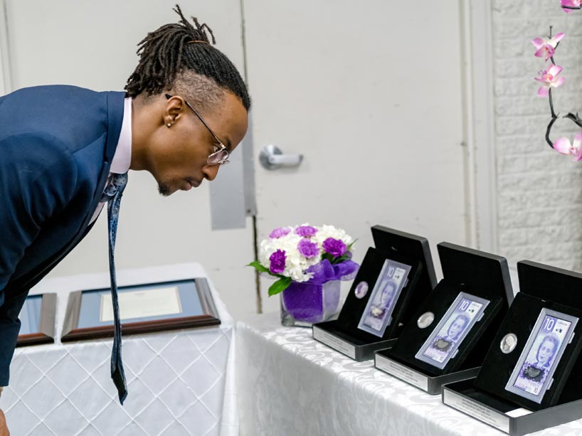 A man bending to get a closer look at the $10 bill with Viola Desmond on it
