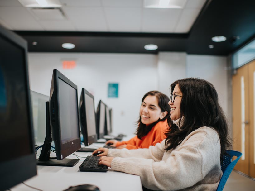 A woman types on a computer while a peer looks at her screen