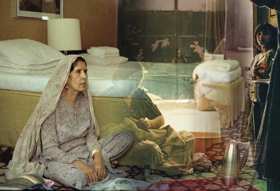 A woman sits on the floor next to a bed facing two family members