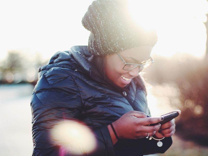 A woman looks down at her phone outside in the sun.