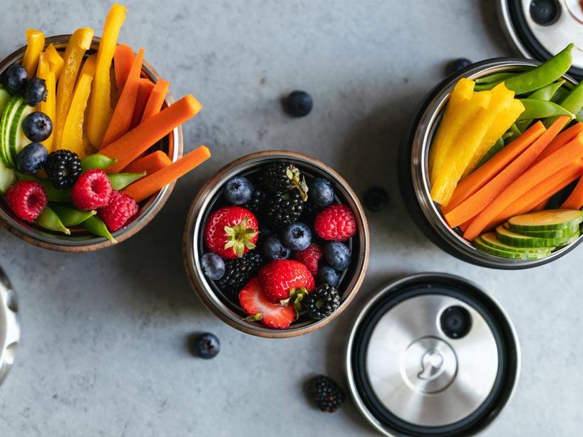fresh, sliced fruits and vegetables in metal containers placed on a counter