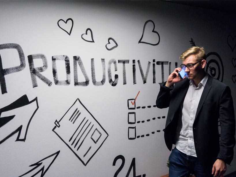 Young man with a phone walks by a white board that says productivity.