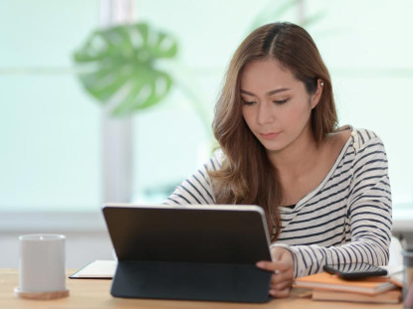 A young woman sitting at a table with a tablet. 