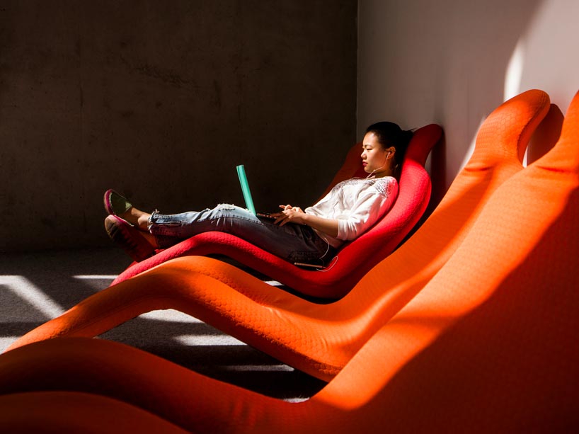 young woman sits in lounge chair using laptop