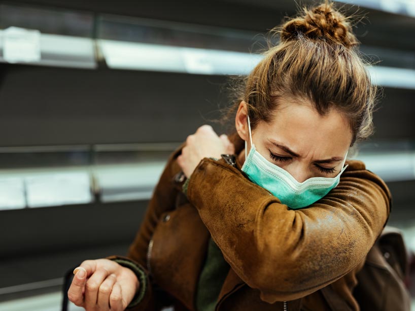 A woman wearing a mask coughs into her elbow