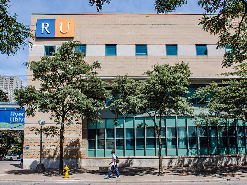 Young man, wearing mask and backpack walks in front of building with RU sign