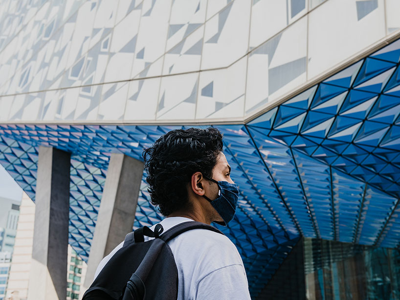 A person in a mask stands facing the Student Learning Centre at Ryerson