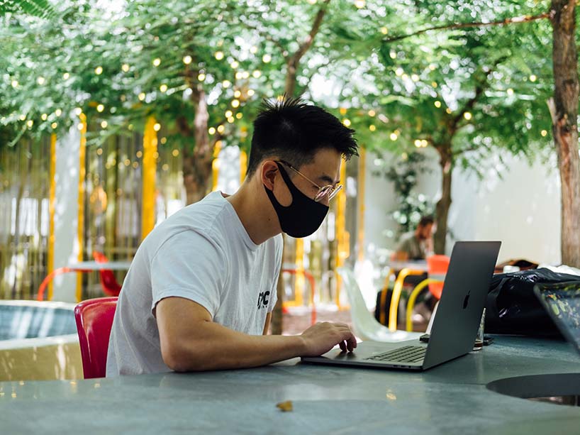 Student sitting outside with laptop and mask on. 