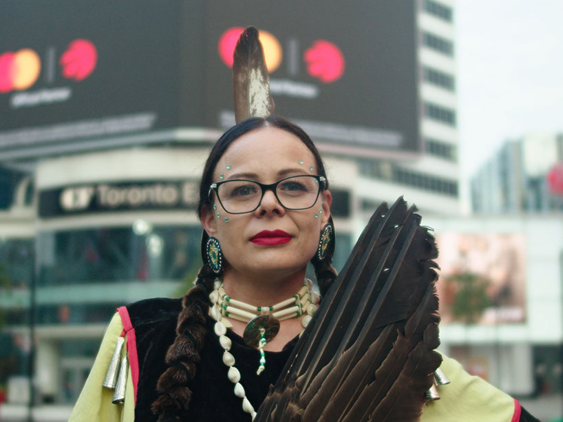 An Indigenous dancer wearing full regalia stands in front of the Eaton Centre