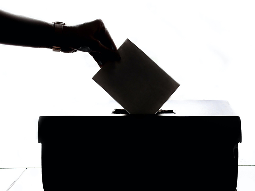 silhouette of a forearm dropping a ballot into ballot box