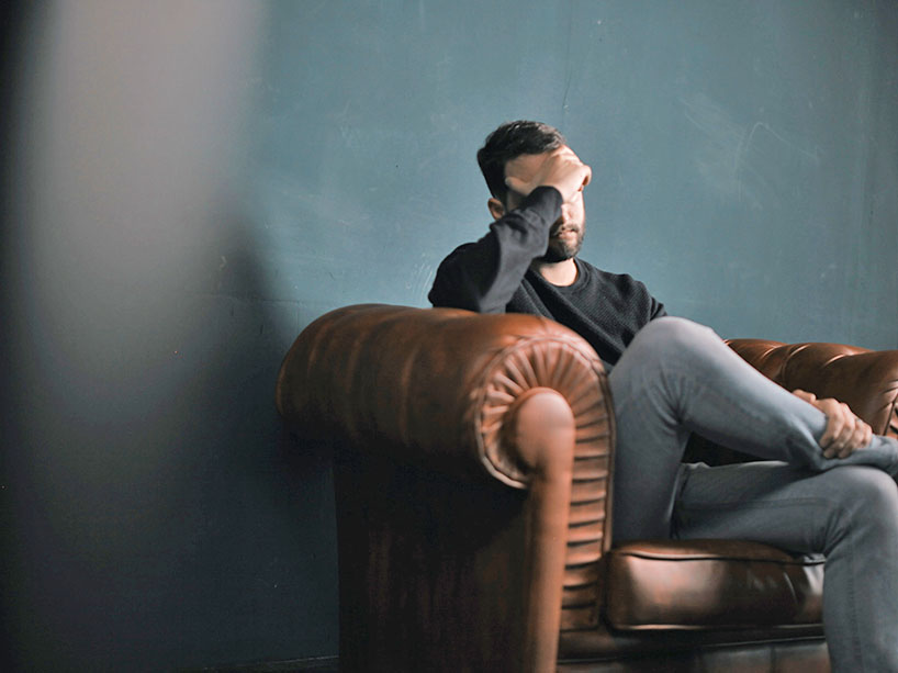 A man sits on a couch with his head in the palm of his hands