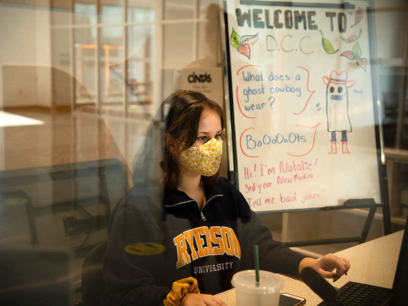 A young woman in a Ryerson sweatshirt sits at the desk with a sign beside her that says Welcome to the DCC