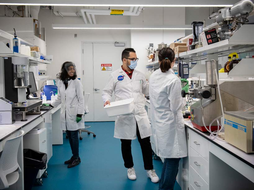 Two women and a man wearing masks stand in a research lab.