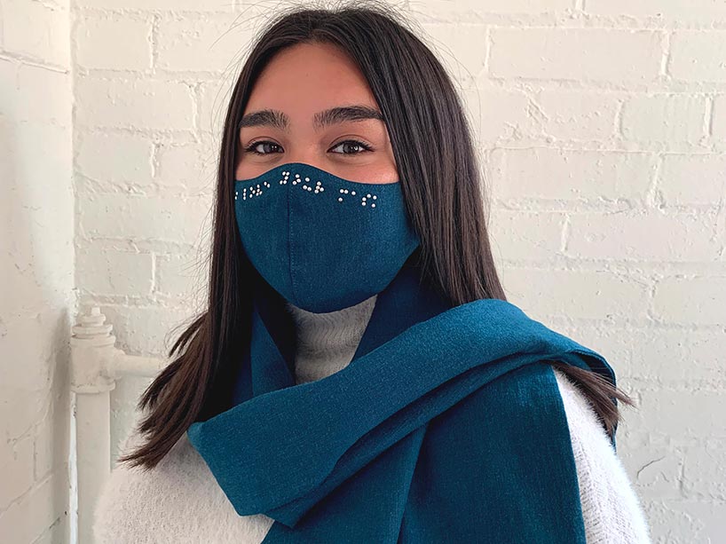 a young woman wears a blue face mask and matching scarf which have braille in crystal beads on the edge of the material