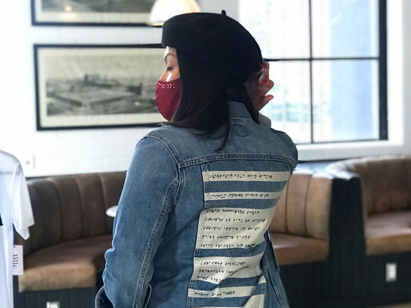 A person wearing a denim jacket with braille text written on the back of it