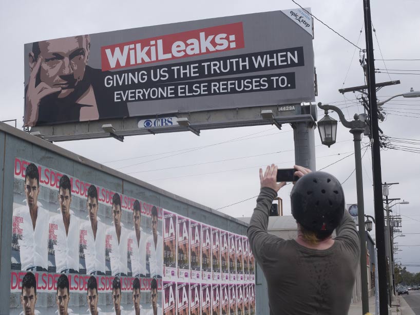 A pedestrian takes a photo of a billboard with WikiLeaks on it, stating Giving us the truth when everyone else refuses to.