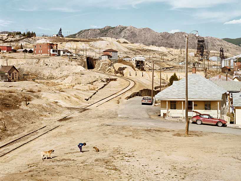 A young person plays with two dogs in a dusty Montana town