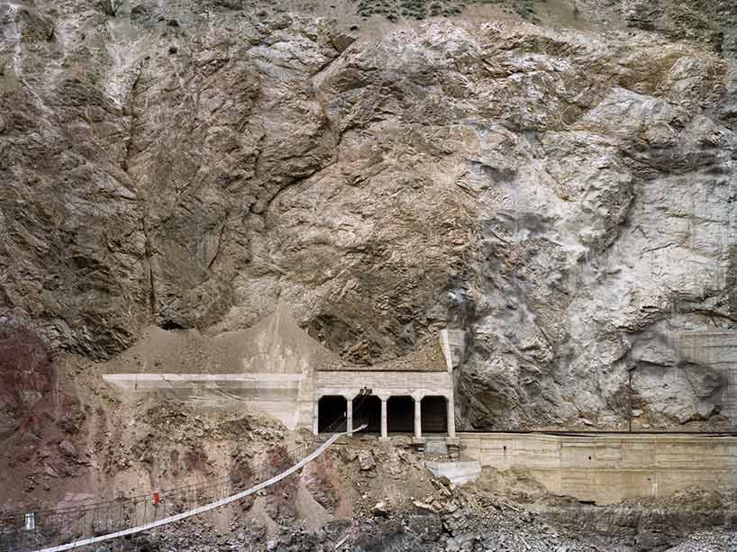 A suspended walking bridge that leads to a railway path cut into a rock face