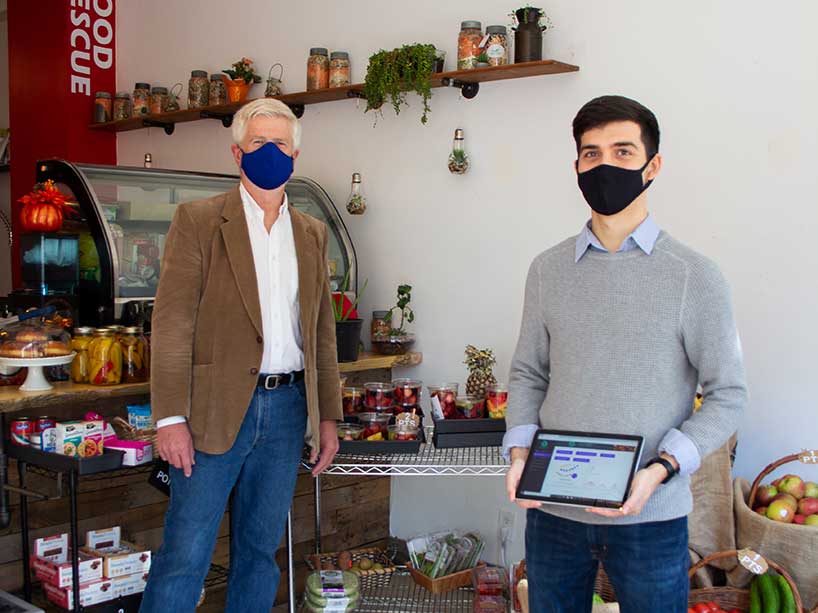 Two men stand in a grocery store, one is holding a tablet.