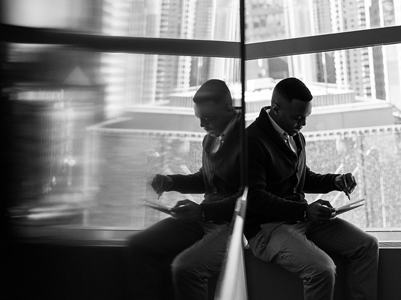 A man sits on a window ledge writing on a pad of paper