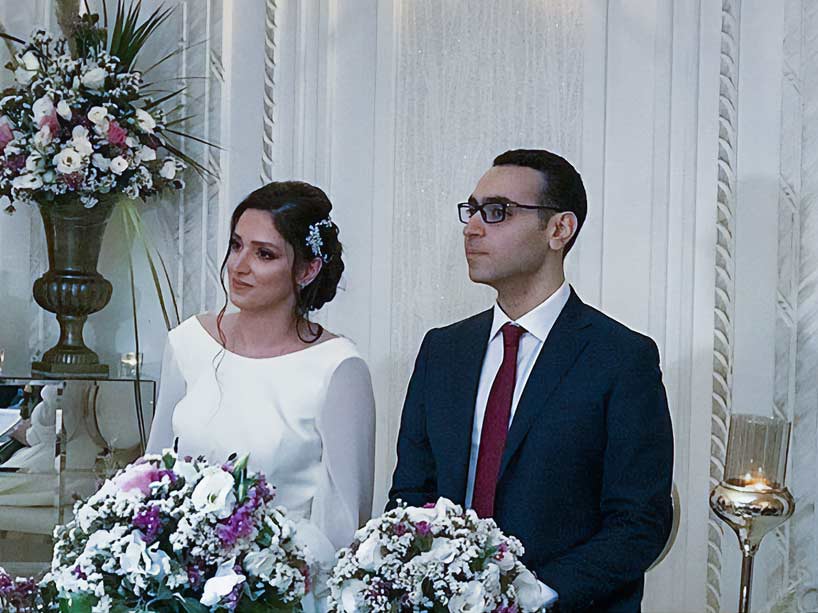 A bride and groom stand side by side in front of flowers on their wedding day.