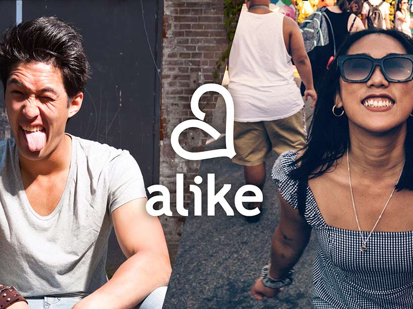A male and female of Asian ethnicity sit on the street smiling at the camera with the word alike superimposed on the image