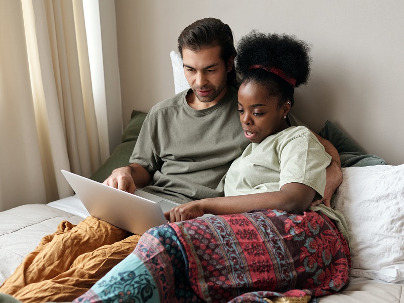 A straight couple reading with a laptop in bed.