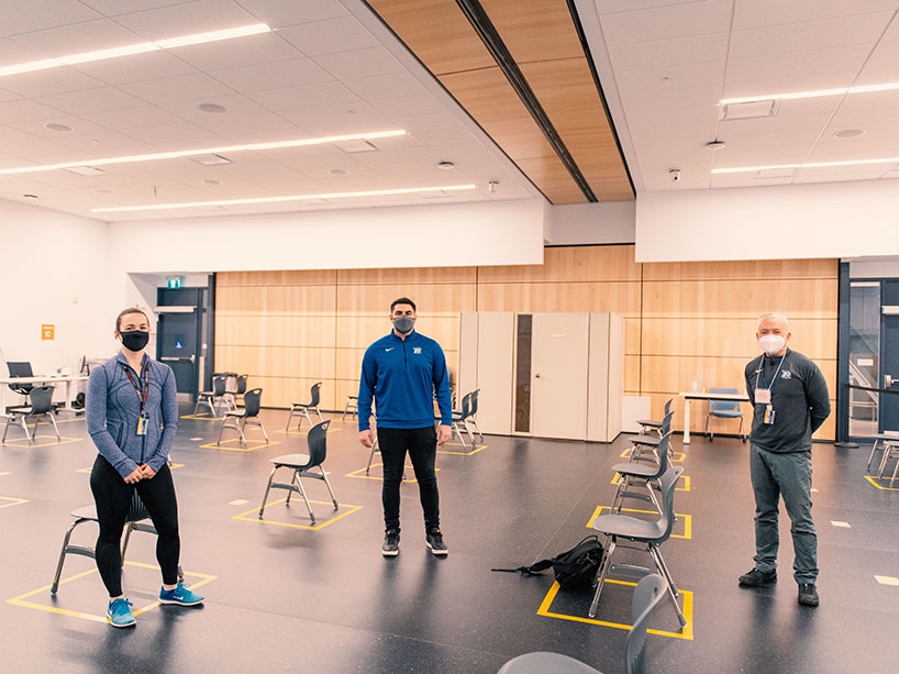 Ryerson staff members wearing masks and standing in a classroom converted into the vaccine clinic’s recovery area.