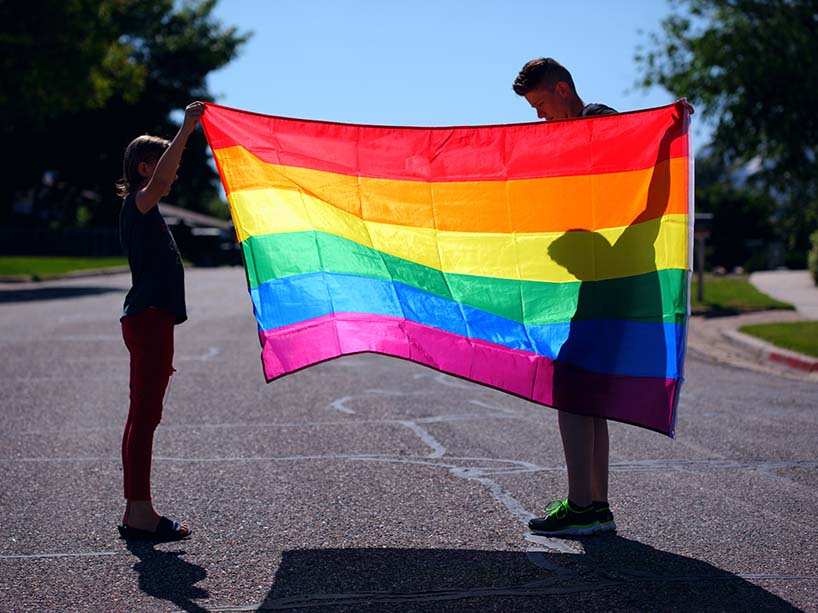 Two people stand outside, each holding one end of a Pride flag.