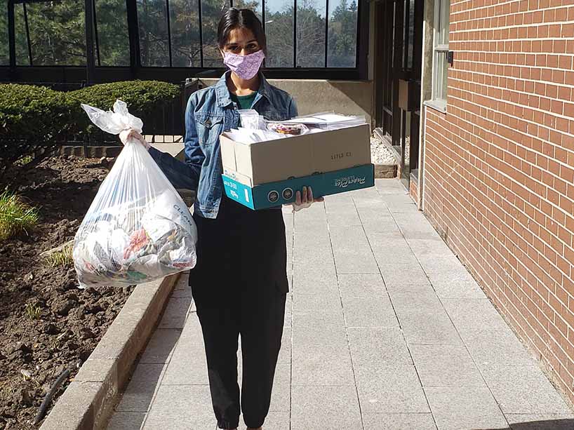 A woman wearing a mask holding a box and bag full of masks. 