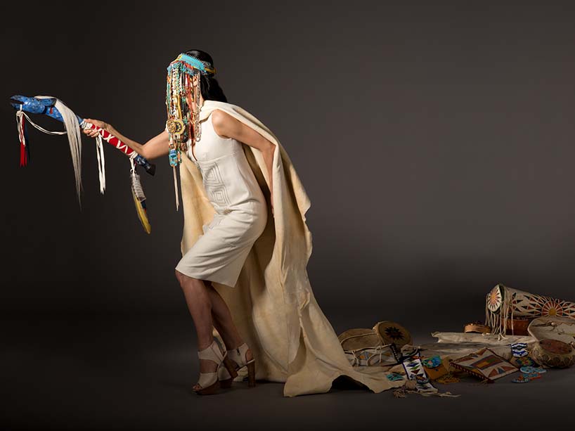 An Indigenous woman wearing a headdress, surrounded by regalia.